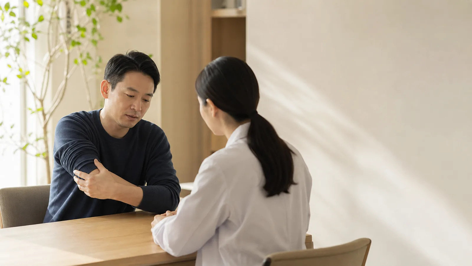 東亞男性在諮詢室輕觸手肘並與專業人員交談